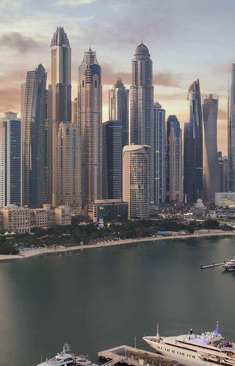 Panoramic sunset view of luxury yachts docked at Dubai Marina surrounded by towering skyscrapers