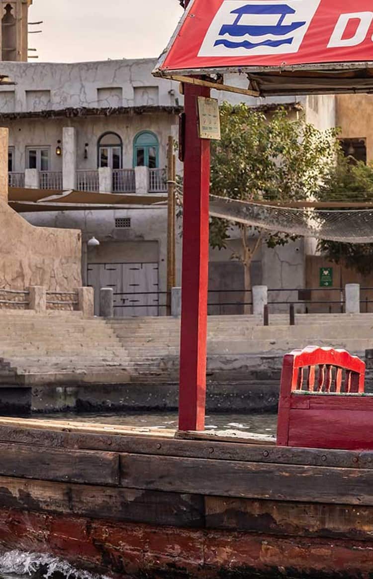 A couple enjoying a ride on a traditional wooden abra boat along Dubai's historic creek with traditional architecture in the background.