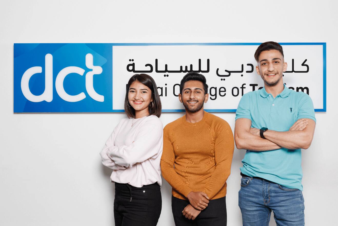 طلاب أمام لوحة تضم شعار كلية دبي للسياحة