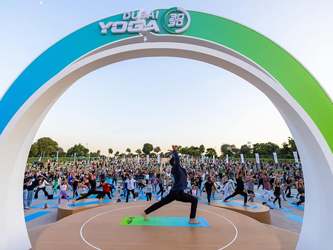 A participant leads an outdoor yoga session beneath the Dubai Yoga event arch