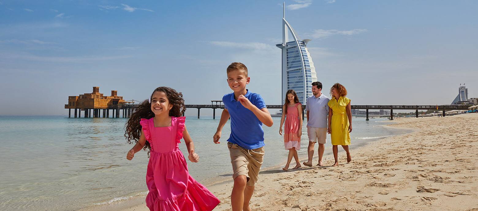 Family running on a beach in front of Burj Al Arab