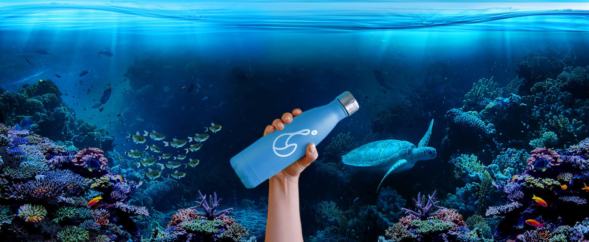 Hand holding a reusable water bottle above a coral reef with a sea turtle swimming nearby